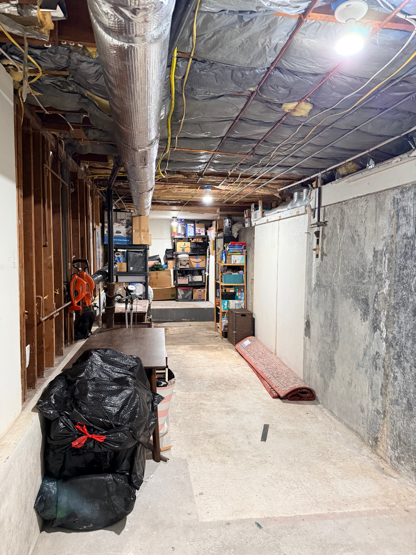 Basement hallway after (second angle): cleared out and walkable, trash bags staged for removal